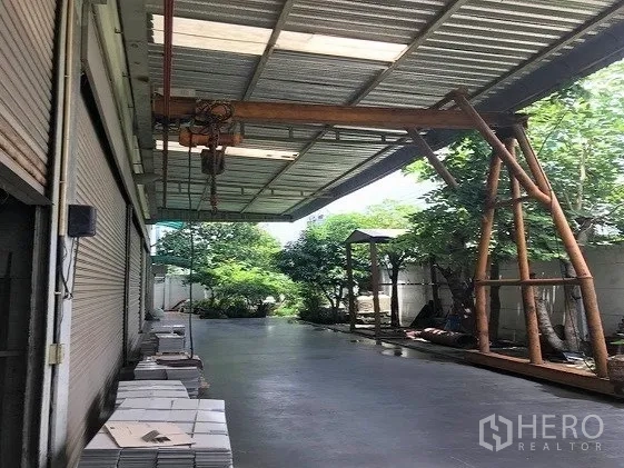 Factory for sale in Khlong Luang, Pathum Thani - Covered loading bay with concrete floor, gantry hoist and trees along the side yard.