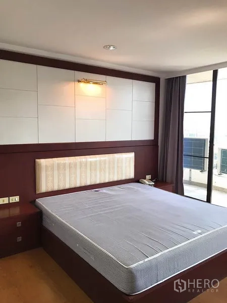 Condominium for rent or sale in Watthana, Bangkok - Master bedroom with upholstered headboard, wood floors and sliding door to balcony.