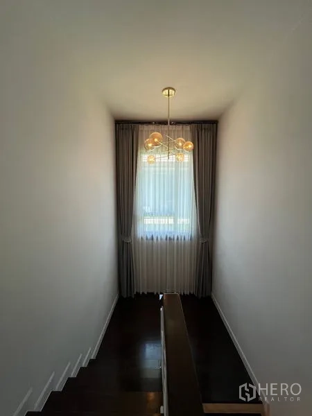 Detached House for rent in Bang Kapi, Bangkok - Staircase landing with modern chandelier and tall curtained window.