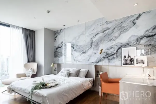 Condominium for rent in Khlong Toei, Bangkok - Primary bedroom with marble accent wall, desk area, lounge chair, and panoramic city view.