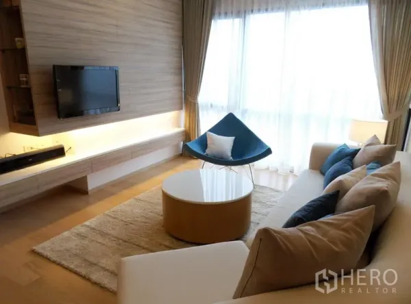 Condominium for rent in Phaya Thai, Bangkok - Bright living room with sofa, TV feature wall, round coffee table and big window with sheer curtains.