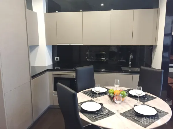 Condominium for rent in Watthana, Bangkok - Contemporary kitchen with L-shaped cabinetry, black stone countertops, built-in appliances and a round dining table.