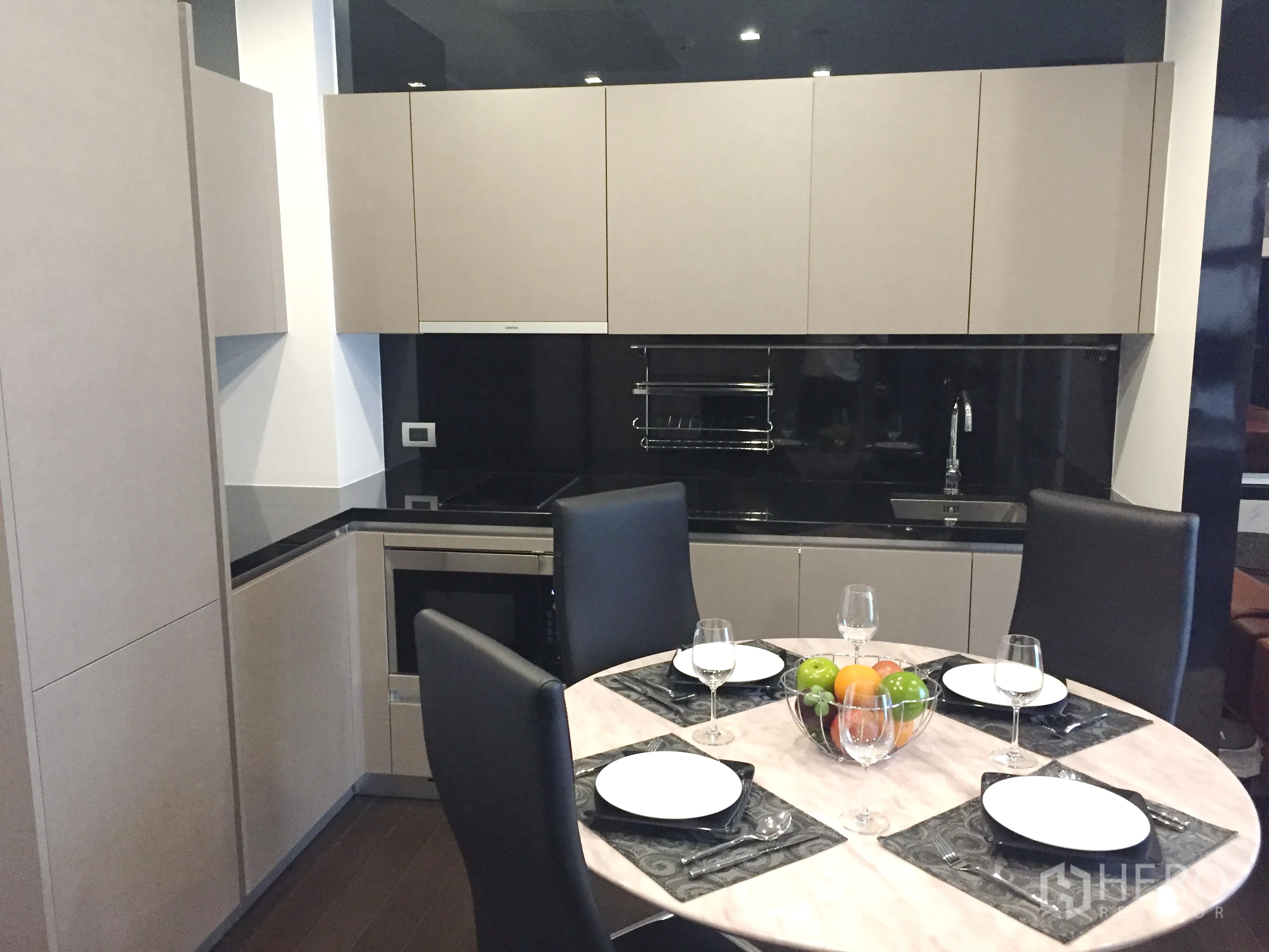 Condominium for rent in Watthana, Bangkok - Contemporary kitchen with L-shaped cabinetry, black stone countertops, built-in appliances and a round dining table.