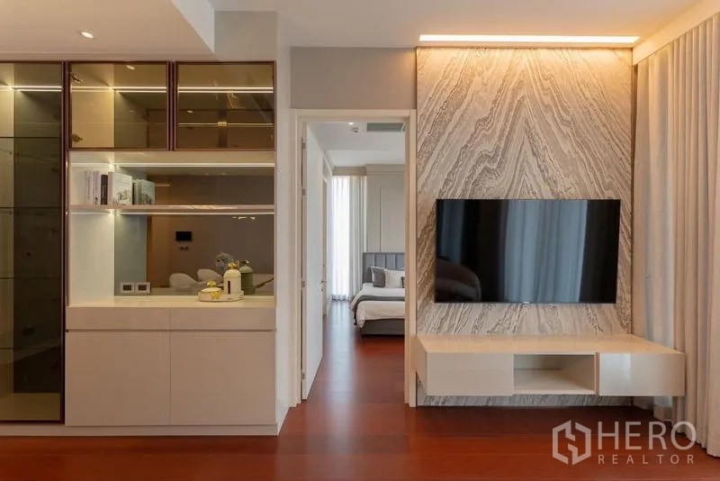 Condominium for rent in Watthana, Bangkok - Feature TV wall with stone pattern paneling beside hallway leading to the bedroom.
