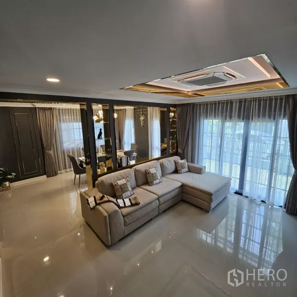 独立式住宅 出租在Bang Phli, Samut Prakan - 明亮客厅，转角沙发、落地窗帘、亮面地砖与嵌入式吊顶空调。