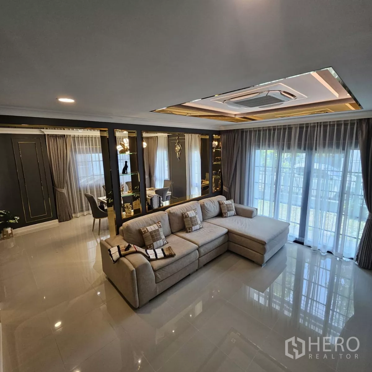 独立式住宅 出租在Bang Phli, Samut Prakan - 明亮客厅，转角沙发、落地窗帘、亮面地砖与嵌入式吊顶空调。
