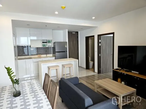 公寓 出租在Bang Na, Bangkok - 开放式客厅与白色厨房，带岛台与电视，Ideo Mobi Sukhumvit 66，近BTS Udom Suk。
