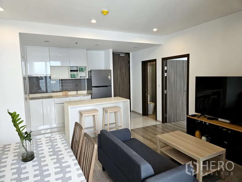 公寓 出租在Bang Na, Bangkok - 开放式客厅与白色厨房，带岛台与电视，Ideo Mobi Sukhumvit 66，近BTS Udom Suk。