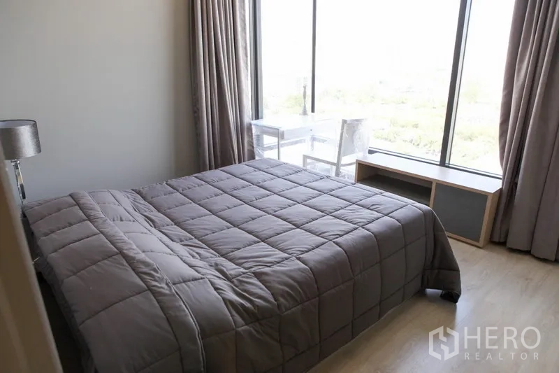 Condominium for rent in Watthana, Bangkok - Bedroom with queen bed, large windows and light wood flooring.