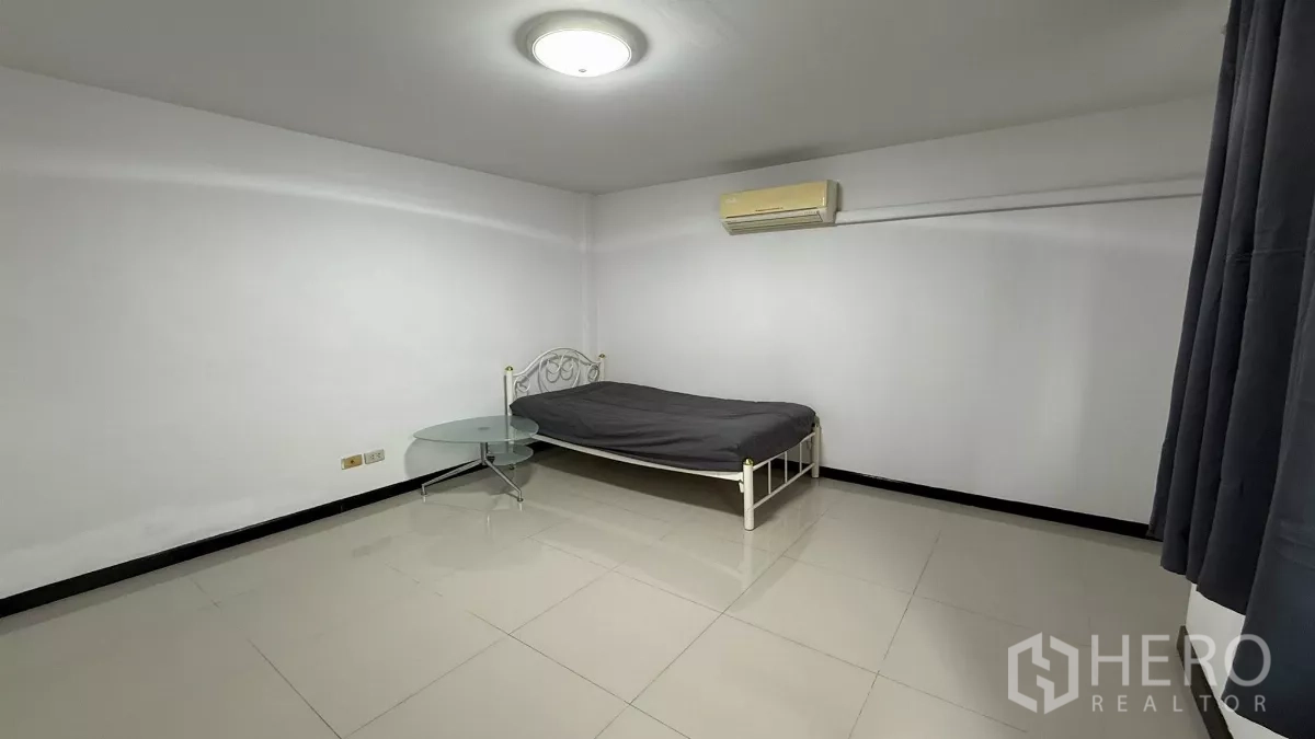 Home Office for rent in Bang Na, Bangkok - Minimal bedroom with single metal bed, round glass table, air conditioner and tiled floor.