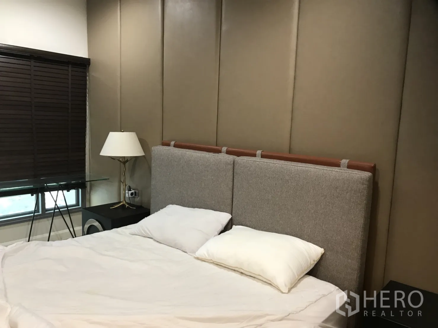 Condominium for rent in Khlong Toei, Bangkok - Cozy second bedroom with upholstered headboard, bedside lamp and window with wooden blinds.