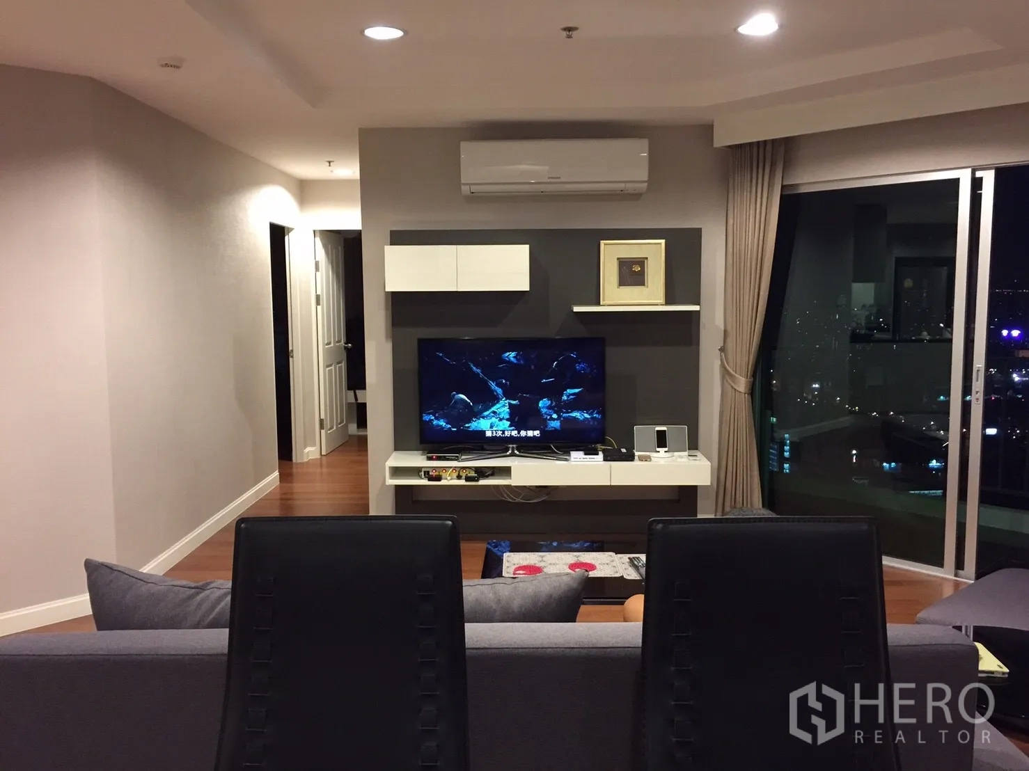 คอนโด ให้เช่าในHuai Khwang, Bangkok - มุมห้องนั่งเล่นหันไปทางทีวีและประตูกระจกบานเลื่อน พร้อมวิวเมืองยามค่ำ