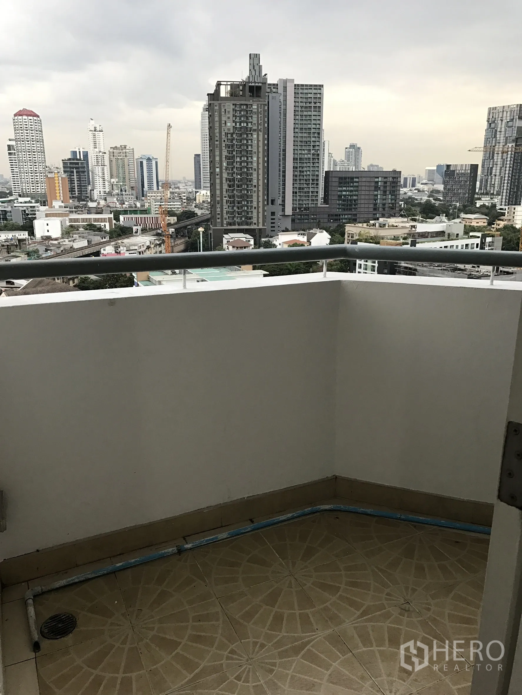 Condominium for rent in Khlong Toei, Bangkok - Balcony with railings overlooking Bangkok skyline on a cloudy day.