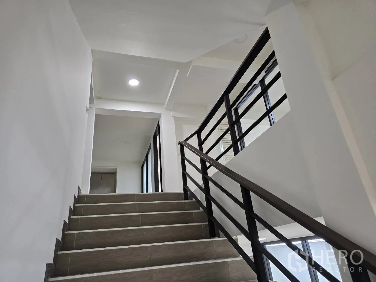 Home Office for rent in Chatuchak, Bangkok - Internal staircase with metal handrail in a clean white corridor.