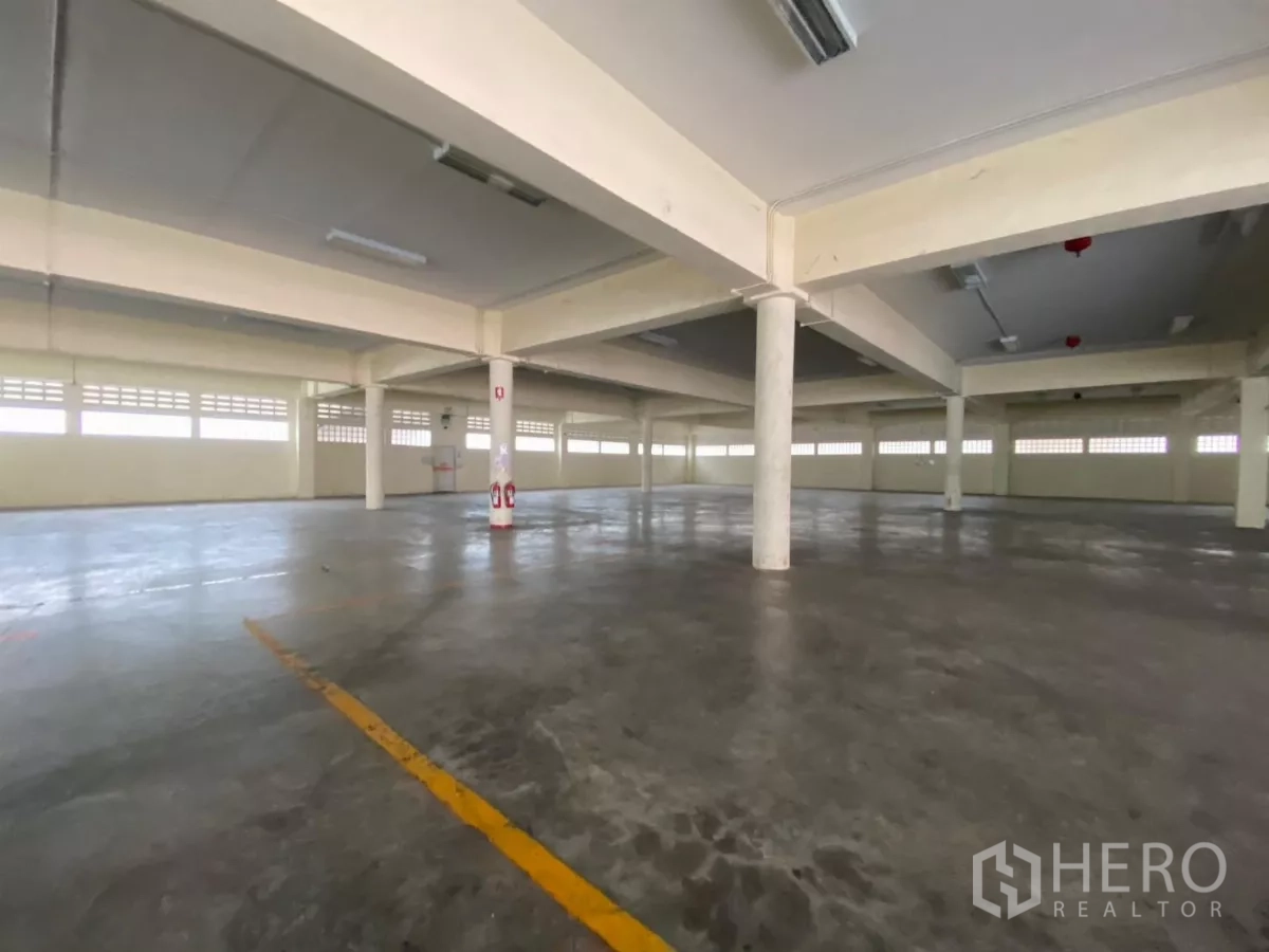 Factory for rent in Khlong Toei, Bangkok - Ground-floor warehouse area with columns, fluorescent lighting, and polished concrete.