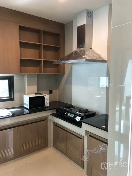 Detached House for rent or sale in Bang Kapi, Bangkok - Fitted kitchen with gas hob, chimney hood, microwave and wood cabinetry.
