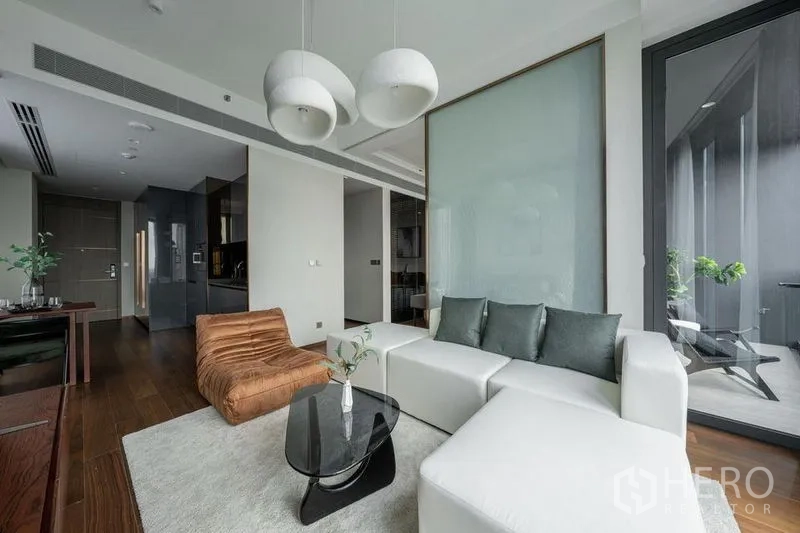 Condominium for rent in Khlong Toei, Bangkok - Living room view toward entrance and sleek kitchen, with partition wall and balcony door.