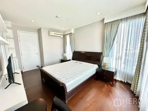 Condominium for rent in Watthana, Bangkok - Spacious master bedroom with wood flooring, sleigh bed, sheer curtains, and air conditioning.