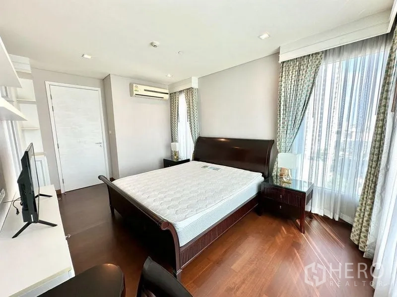 Condominium for rent in Watthana, Bangkok - Spacious master bedroom with wood flooring, sleigh bed, sheer curtains, and air conditioning.