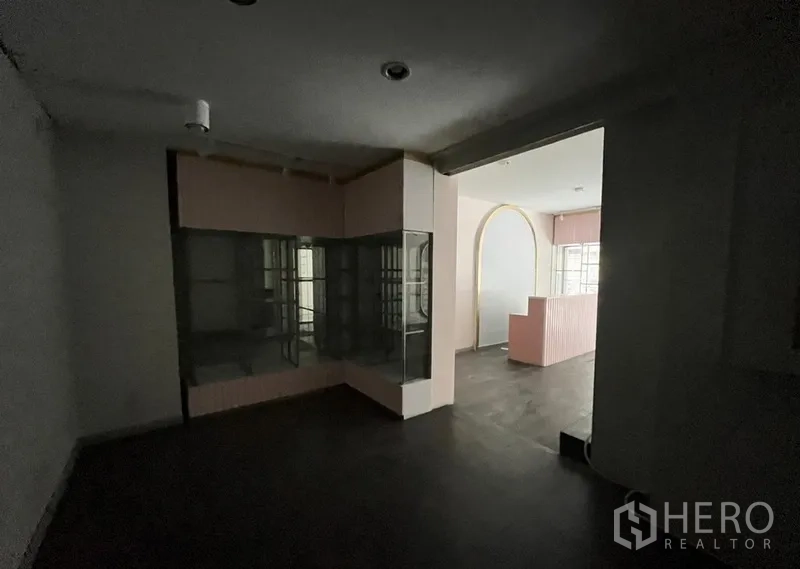 Shophouse for rent in Watthana, Bangkok - Rear room with glass display cabinet and arched opening leading to the front shop area.