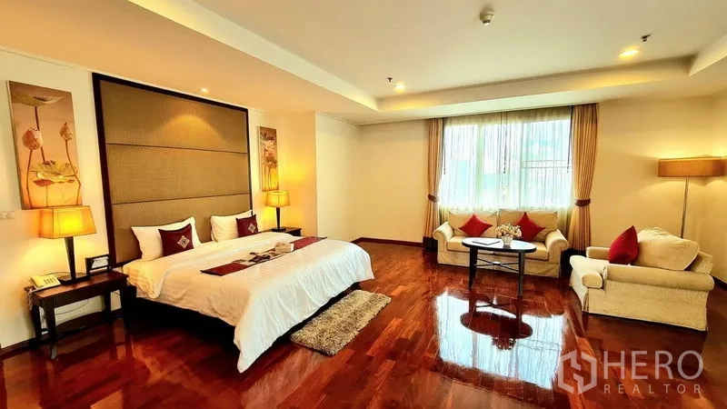 Apartment for rent in Khlong Toei, Bangkok - Spacious master bedroom with king bed, seating area and polished wood floors.