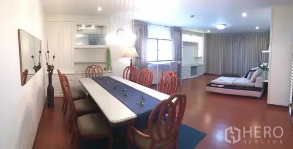Condominium for rent or sale in Din Daeng, Bangkok - Open-plan dining and living area with long marble-top table, wooden chairs, built-in cabinetry and large curtained windows.