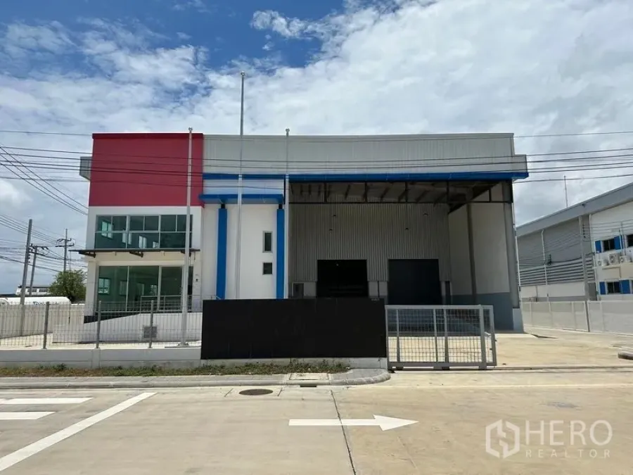 Factory for rent in Mueang Samut Prakan, Samut Prakan - Modern factory exterior with gated entrance, office wing and covered loading bays on a clear day.
