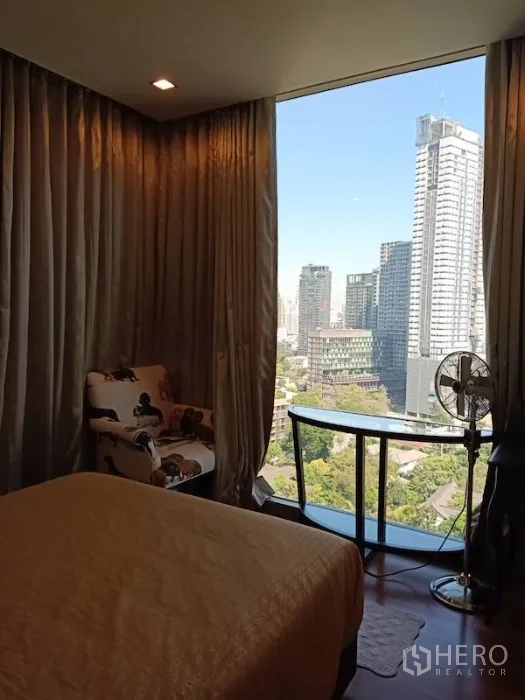 Condominium for rent in Khlong Toei, Bangkok - Bright bedroom with large picture window, city skyline vista, desk and curved glass shelf.