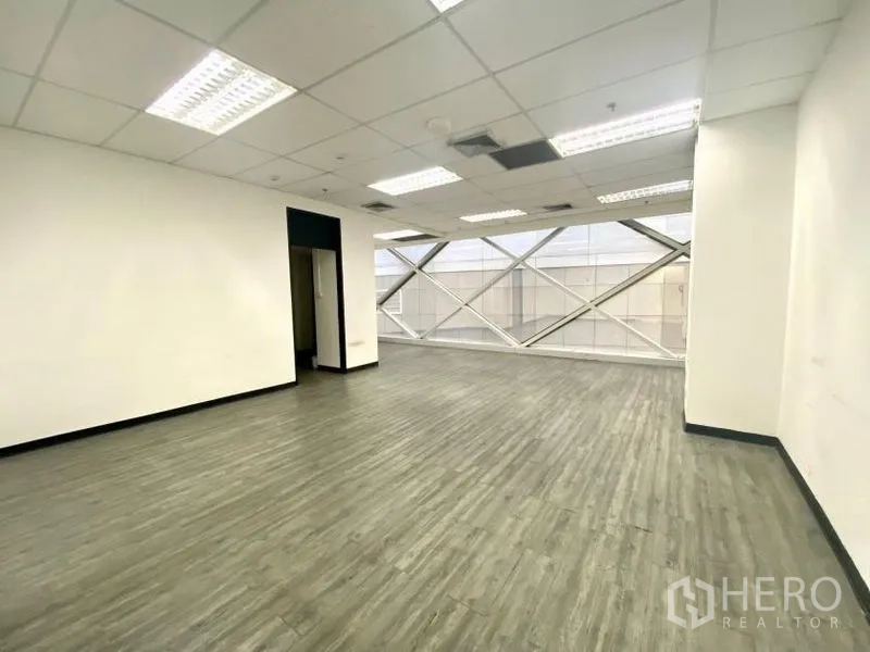 Office Space for rent in Khlong Toei, Bangkok - Bright open-plan office with wood-look vinyl flooring, white walls, grid ceiling, and large diagonal-braced window.