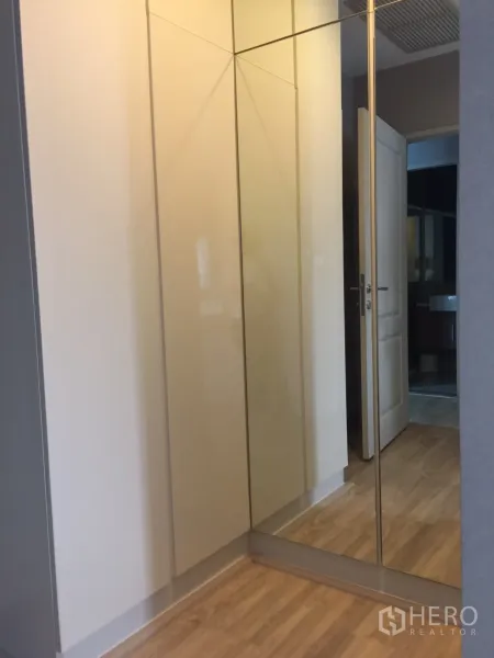 Condominium for rent or sale in Bangkok - Corner wardrobe with mirrored doors and wood flooring near the bathroom entrance.