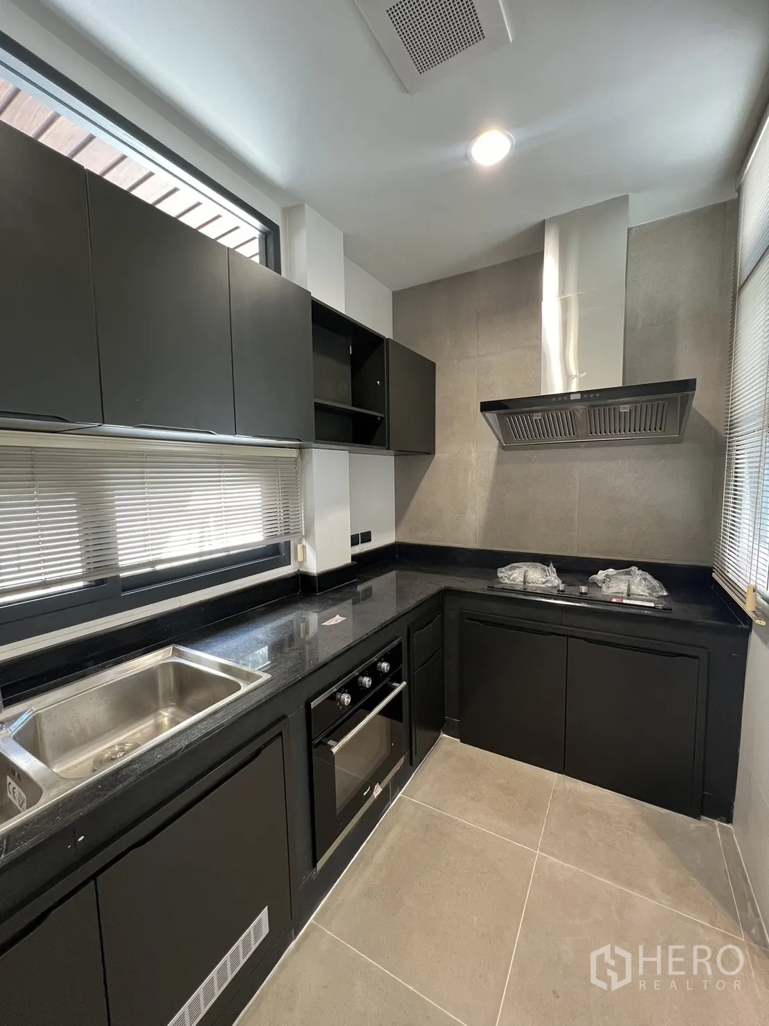 Detached House for rent in Saphan Sung, Bangkok - Modern U-shaped kitchen with black cabinets, stone countertops, built-in oven and stainless range hood.