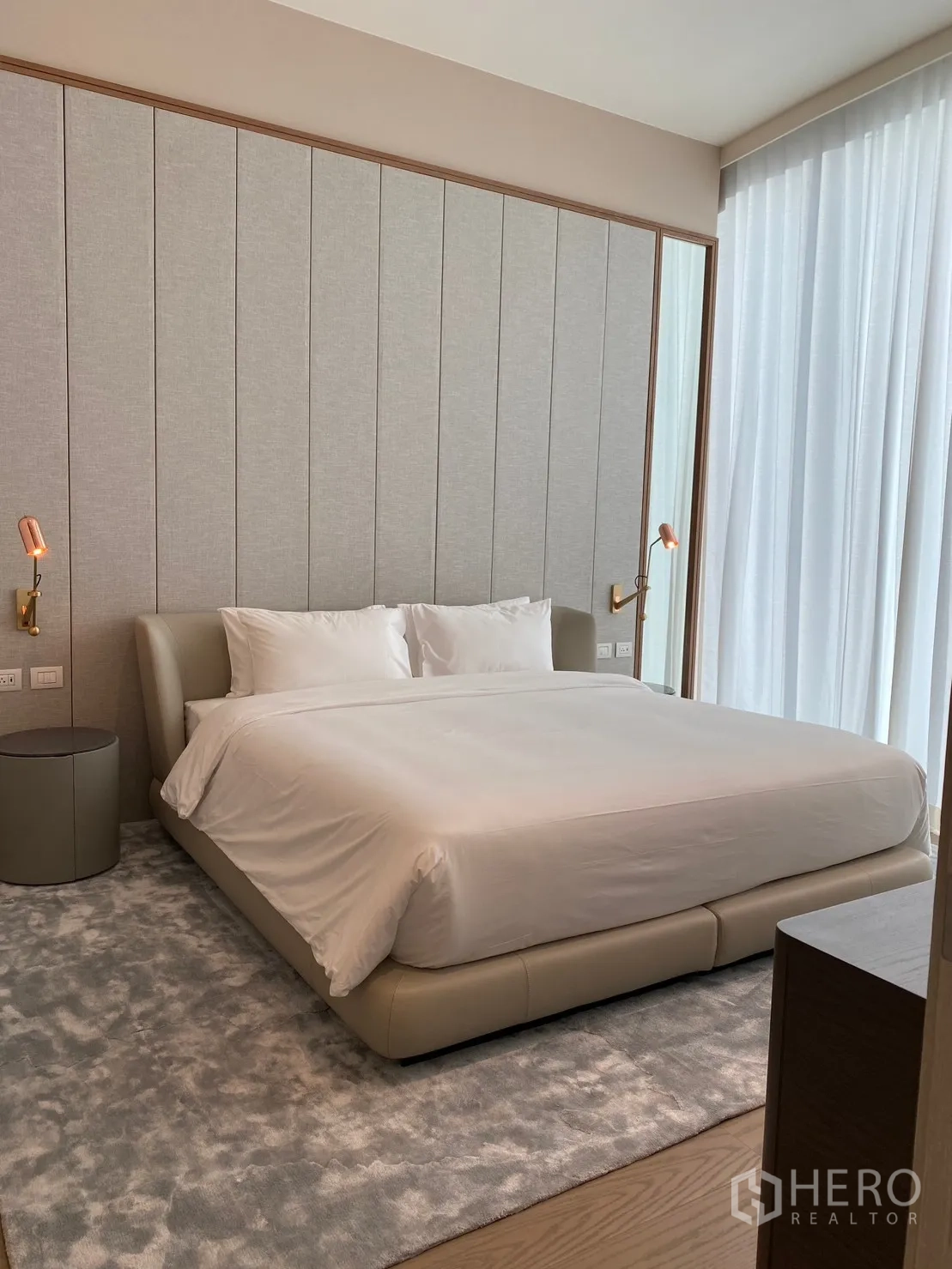 คอนโด for rent in Pathum Wan, Bangkok - ห้องนอนสไตล์หรูพร้อมเตียงหุ้มหนัง ผนังหัวเตียงบิวท์อิน ผ้าม่านสูงจรดเพดาน พรมฟูนุ่ม และโคมไฟข้างเตียงโทนอุ่น