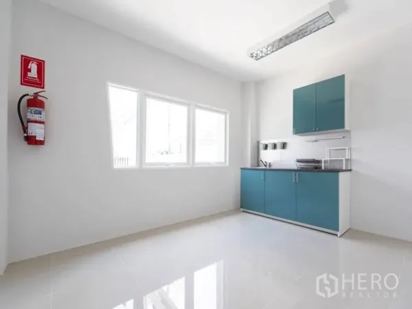 Factory for rent in Bang Bo, Samut Prakan - Compact pantry with teal cabinets, countertop sink, window and wall‑mounted fire extinguisher.