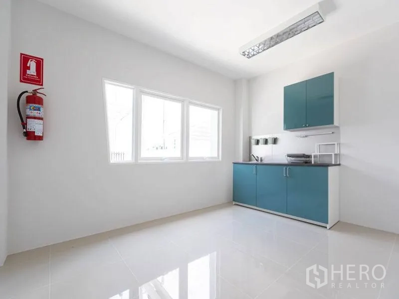 Factory for rent in Bang Bo, Samut Prakan - Compact pantry with teal cabinets, countertop sink, window and wall‑mounted fire extinguisher.