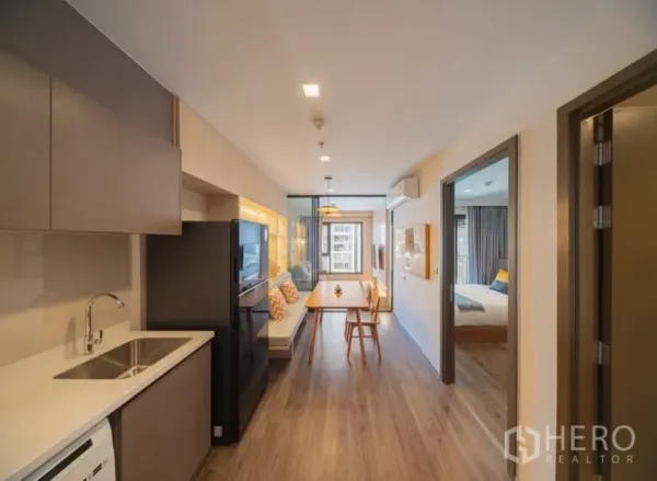 Condominium for rent in Chatuchak, Bangkok - Open-plan kitchen with white countertop, dining table and sliding glass partition leading to the living room in a modern Chatuchak condo.