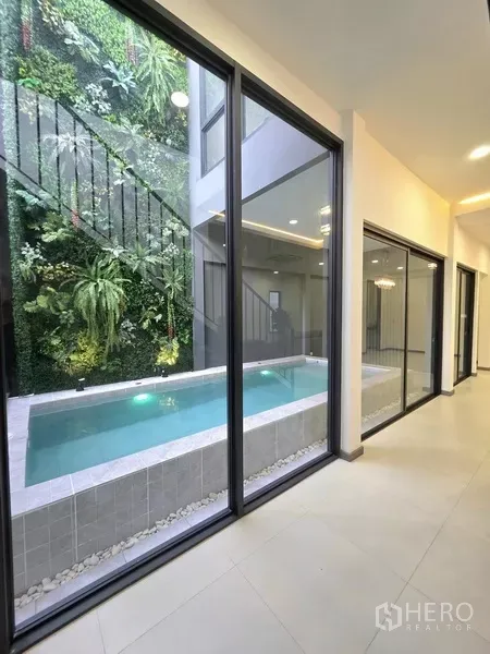 独立式住宅 出售在Khlong Toei, Bangkok - 走廊透过落地玻璃可见泳池及郁郁葱葱的垂直花园。