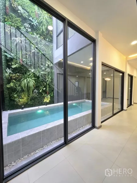 独立式住宅 出售在Khlong Toei, Bangkok - 走廊透过落地玻璃可见泳池及郁郁葱葱的垂直花园。