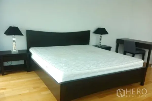 Condominium for sale in Khlong Toei, Bangkok - Primary bedroom with a king-size bed frame, bedside tables with modern lamps, and a work desk on wood flooring.