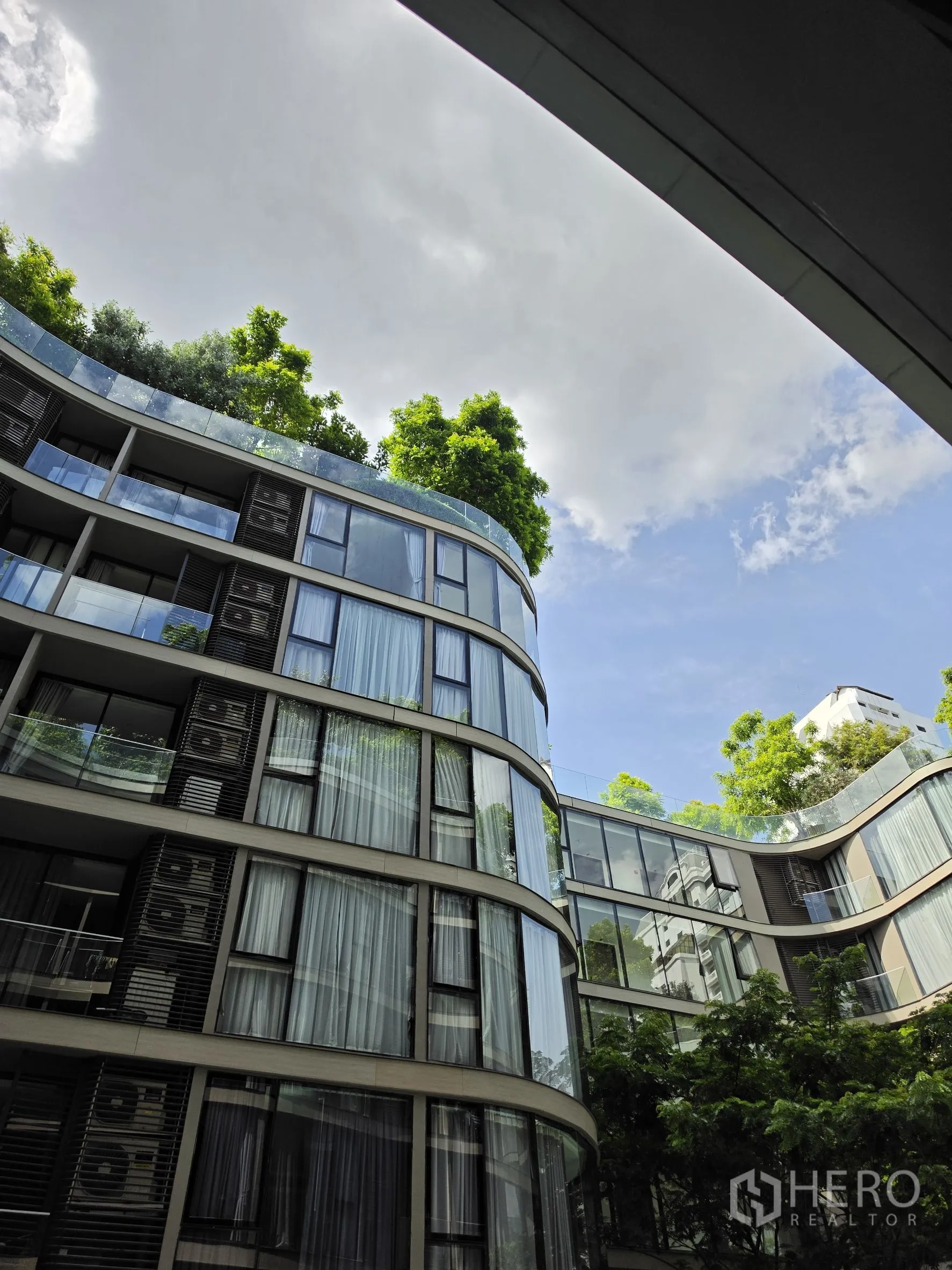 Condominium for rent in Khlong Toei, Bangkok - Modern condominium exterior with curved glass facade and rooftop greenery.