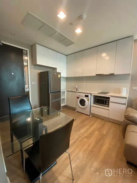Condominium for rent in Bangkok - Modern kitchen with white cabinetry, refrigerator, washing machine, microwave and a glass dining table.