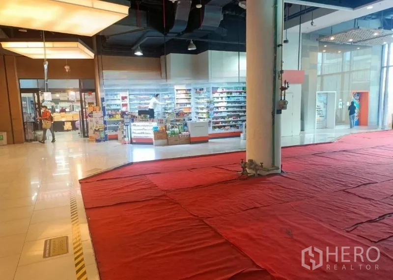 Retail Space for rent in Khlong Toei, Bangkok - Corner retail unit with floor-to-ceiling glass frontage, high black ceiling, central pillar and red protective flooring inside a shopping mall.
