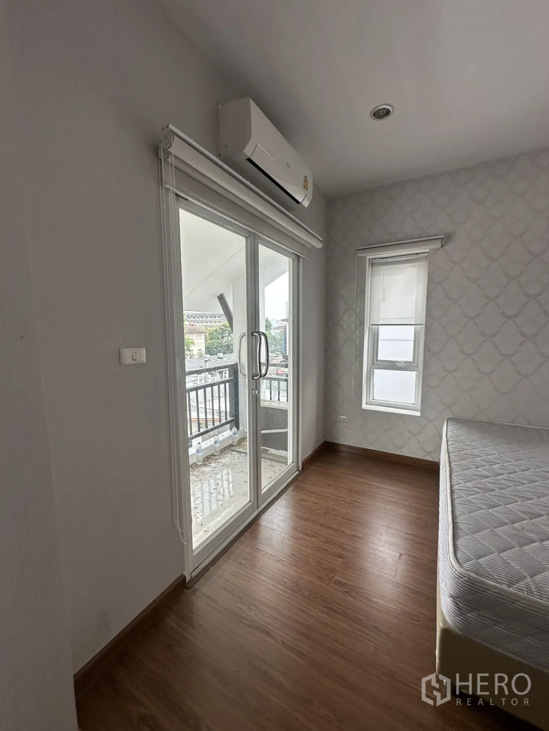 โฮมออฟฟิศ for rent in Watthana, Bangkok - ห้องนอนขนาดกะทัดรัด พื้นไม้ ประตูกระจกบานเลื่อนไปยังระเบียง มู่ลี่ และเครื่องปรับอากาศแขวนผนัง