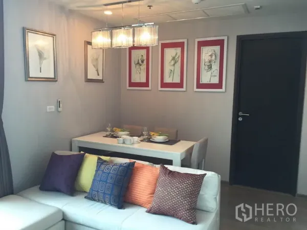 公寓 出租在Ratchathewi, Bangkok - 起居区配转角沙发与彩色抱枕，旁为明亮餐桌与墙面装饰画。