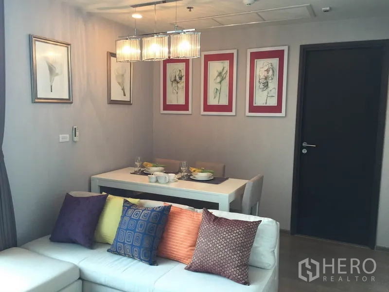 公寓 出租在Ratchathewi, Bangkok - 起居区配转角沙发与彩色抱枕，旁为明亮餐桌与墙面装饰画。
