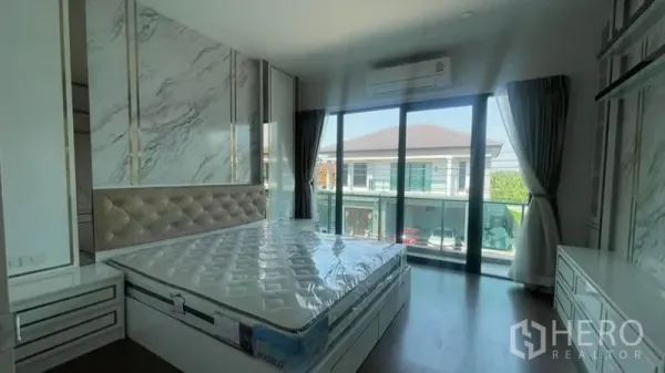 Detached House for rent or sale in Prawet, Bangkok - Primary bedroom with marble accent wall, built-in storage and sliding glass doors to a balcony.