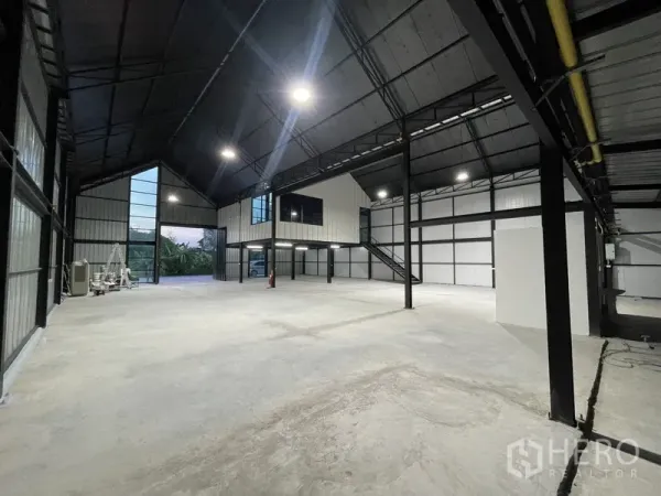 Warehouse for rent in Bueng Kum, Bangkok - Double-height warehouse hall with glass-fronted mezzanine office, wide entry and bright ceiling lights.