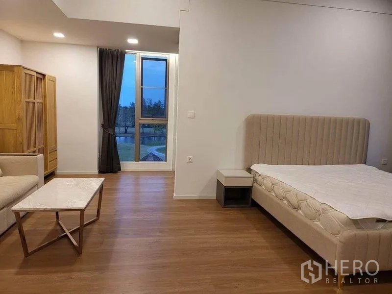 Detached House for rent in Saphan Sung, Bangkok - Spacious bedroom with wood floors, upholstered bed, sofa and marble coffee table facing a tall window with garden view.