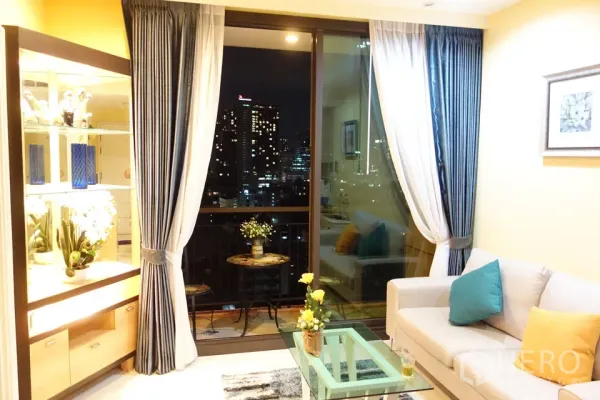 公寓 出租在Khlong Toei, Bangkok - 客厅配玻璃茶几与沙发，落地窗通往阳台，夜景城市天际线。
