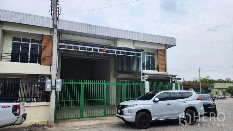 โรงงาน ให้เช่าในSamut Sakhon - ด้านหน้าโรงงานสองชั้นสมัยใหม่ ประตูรั้วสีเขียวและที่จอดรถกว้าง