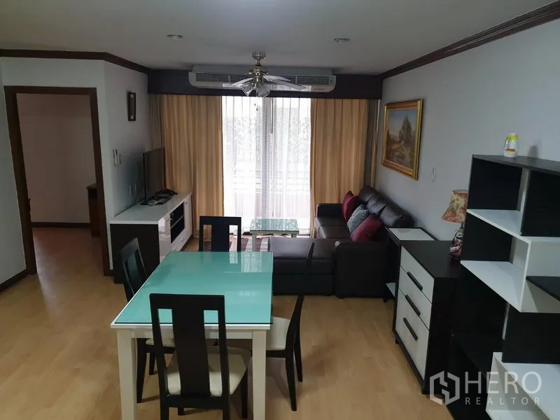 Condominium for rent in Watthana, Bangkok - Open-plan living and dining room with a glass-top table, TV console, sofa set, and balcony doors with curtains.